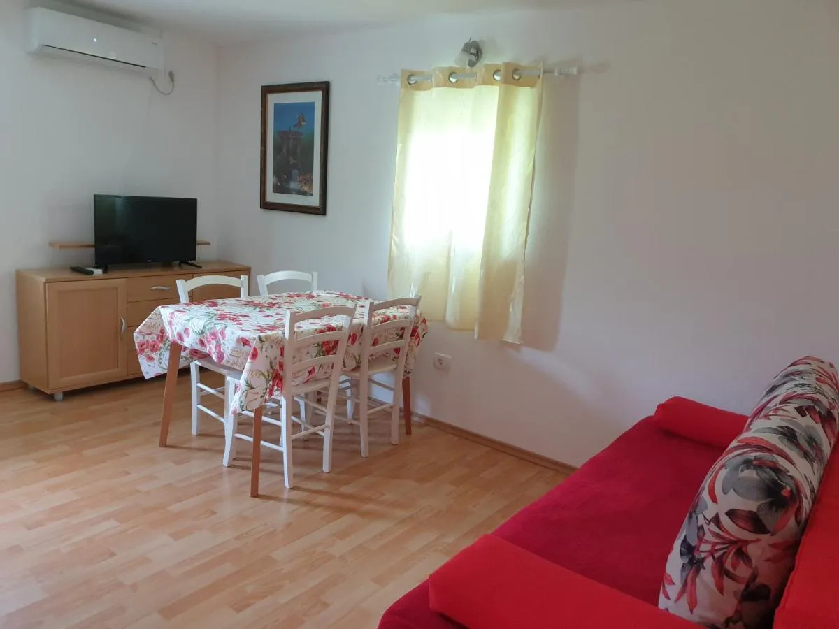 Dnevna soba apartmaja s teraso: rdeč raztegljiv kavč, jedilna miza z belimi stoli, televizor in klima