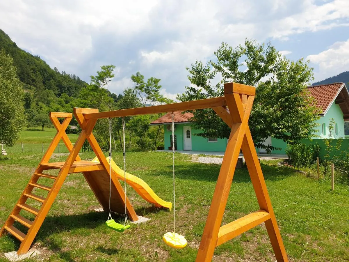Rumeni sedeži gugalnice in rumen tobogan, zadaj mintno zelena hiša